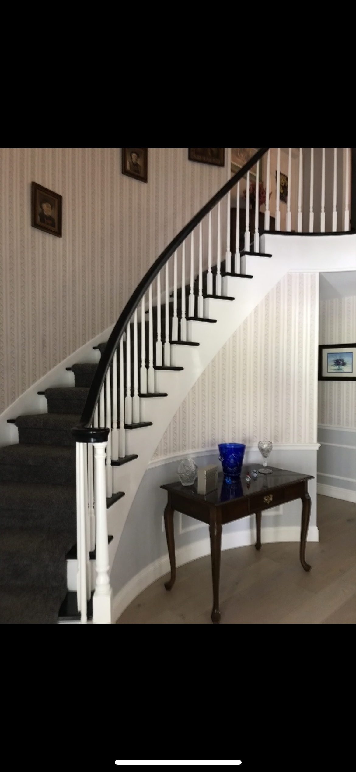 Curved staircase with dark handrail and white balusters. Wooden table with blue vase and glasses.