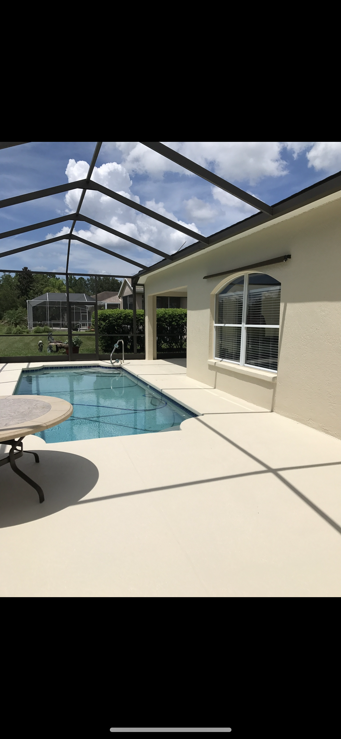Pool area with screened enclosure, pool, table, and house with an arched window.