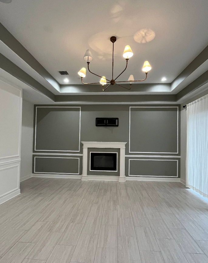Empty living room with fireplace, gray accent wall with white trim, chandelier, and light wood flooring.