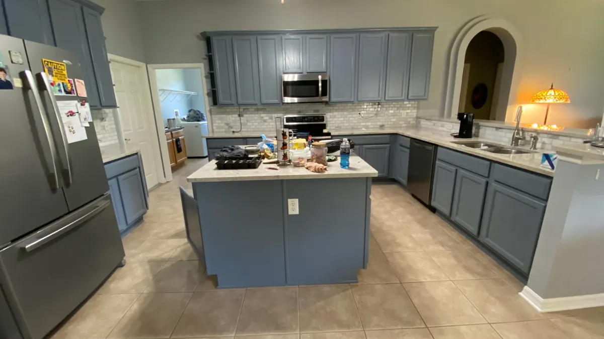Blue-painted kitchen with island, stainless steel appliances, and beige tile floor.