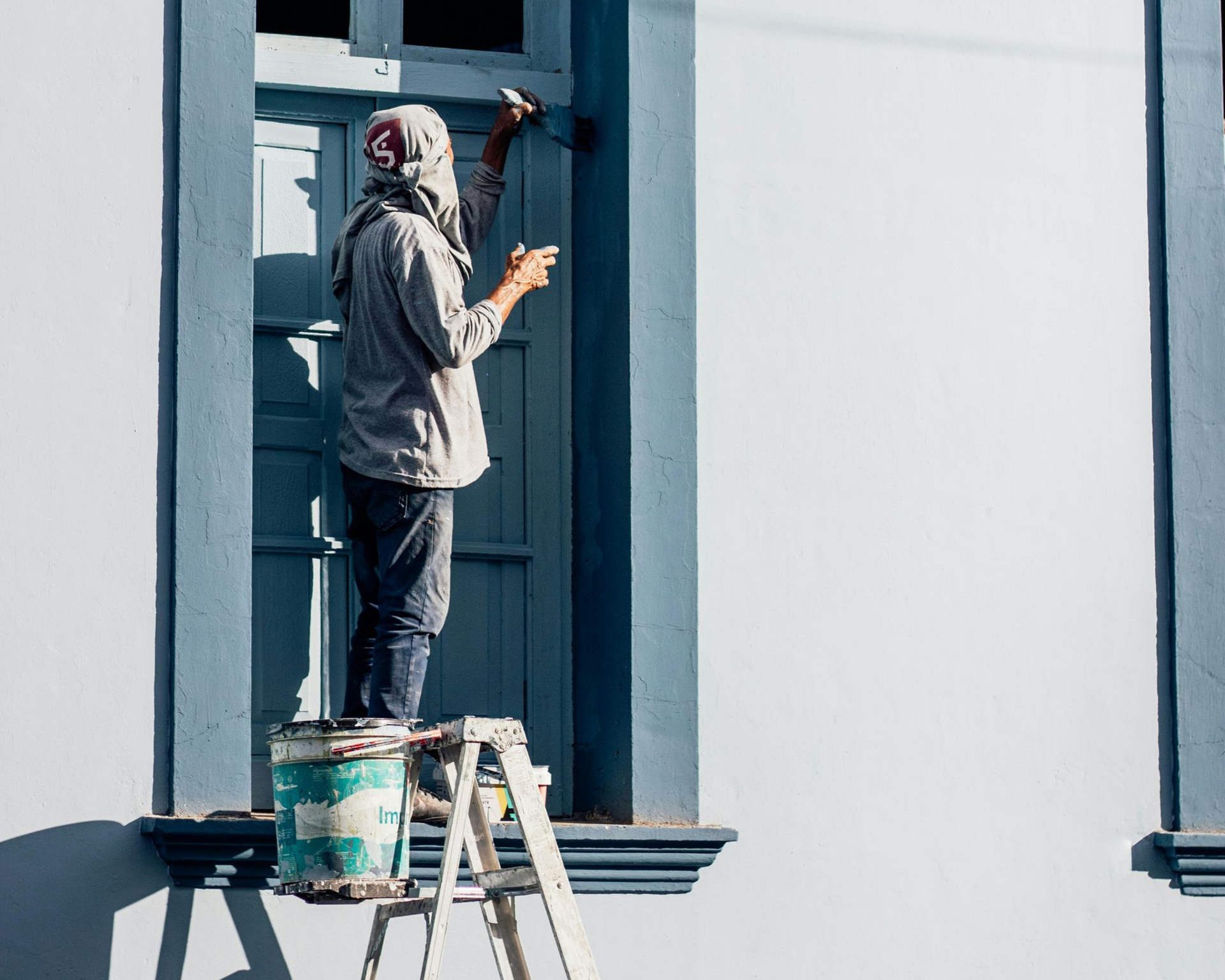 Painter on a ladder painting a window frame on a white building