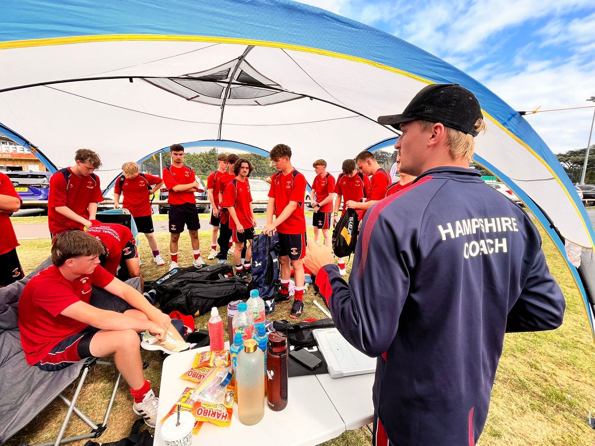 Coach speaking to a red-clad team under a canopy during a sports huddle
