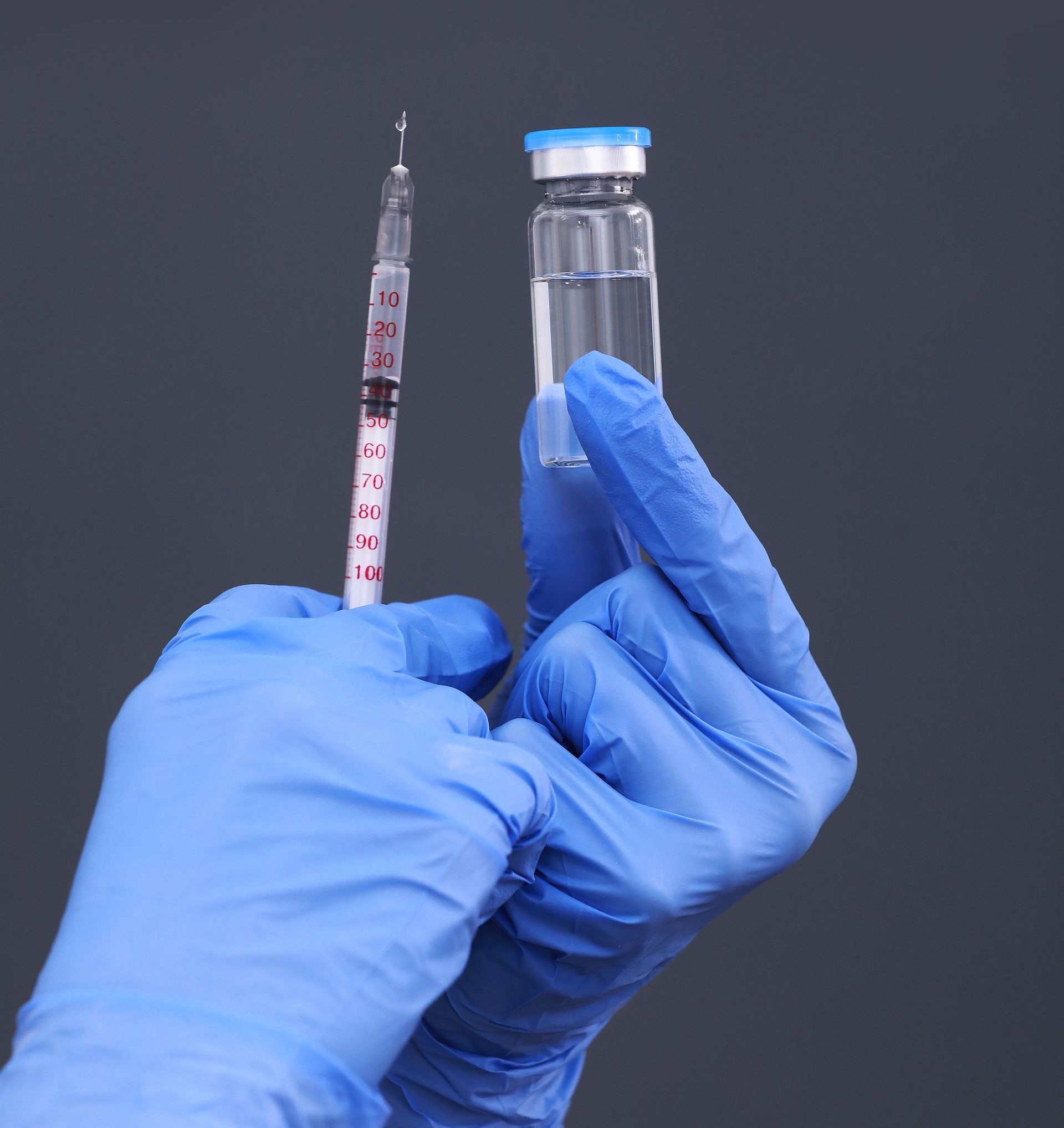 A person wearing blue gloves is holding a syringe and a bottle of liquid.