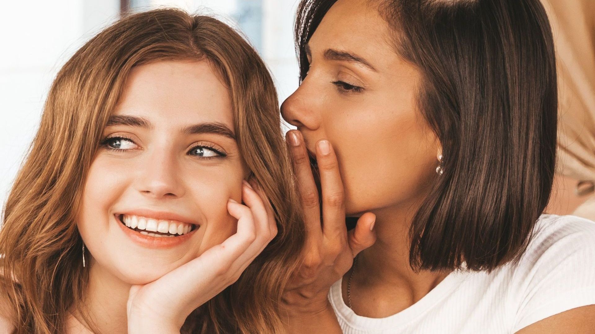 A woman is whispering a secret into another woman 's ear.