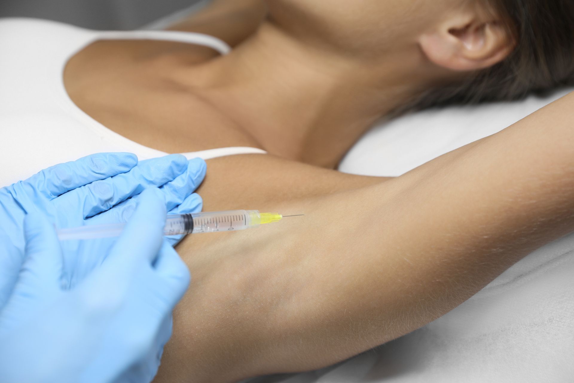 Gloved hand giving an injection into a person’s upper arm