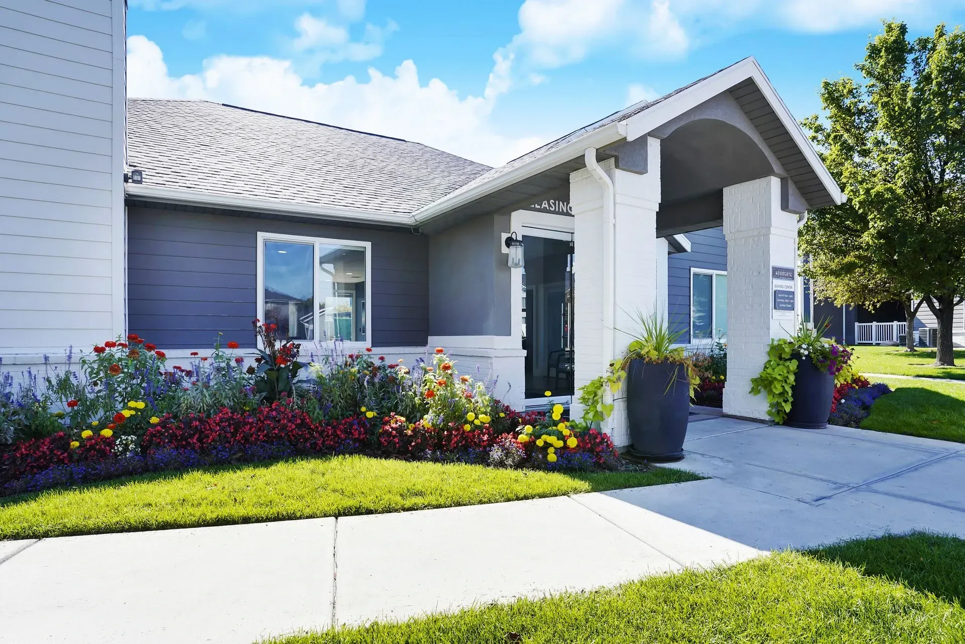 Building entrance with colorful flower beds and lush green lawn.