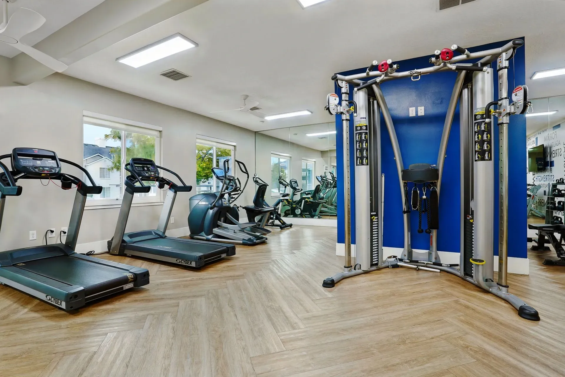 Treadmills and weight machines in a well-lit fitness center with large mirrors.