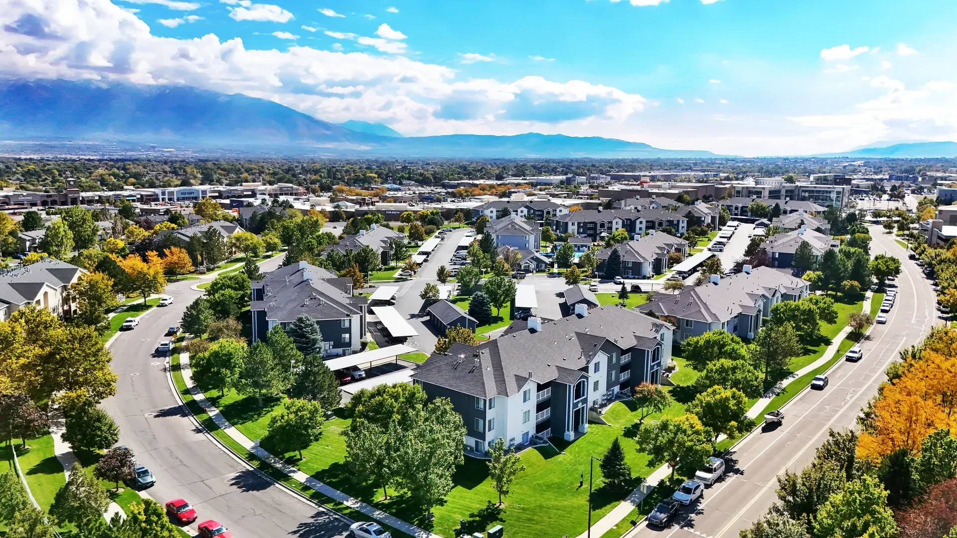 Aerial view of an apartment complex with lush green landscaping and mountains in the background.