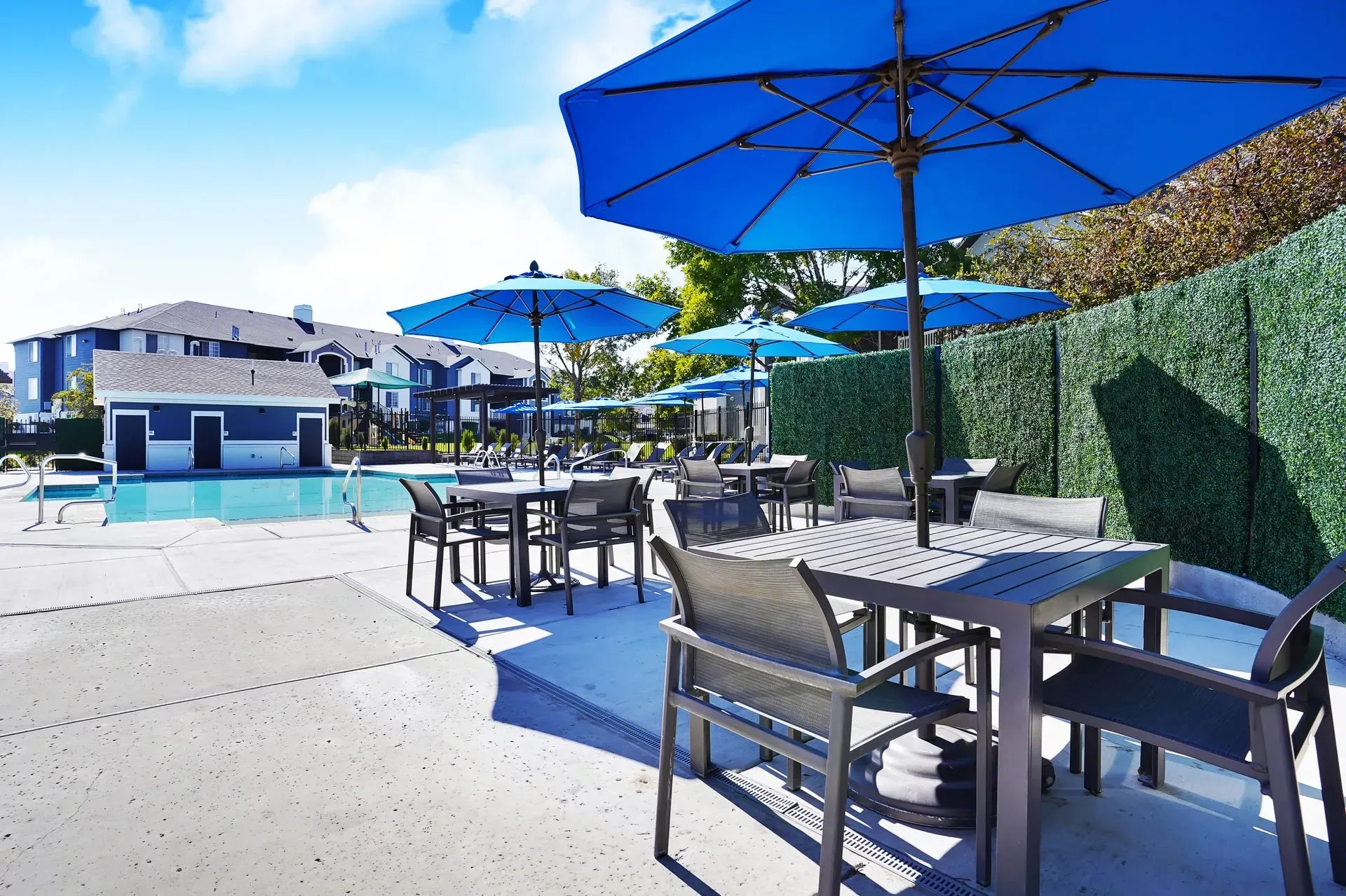 Outdoor swimming pool area with tables and blue umbrellas.