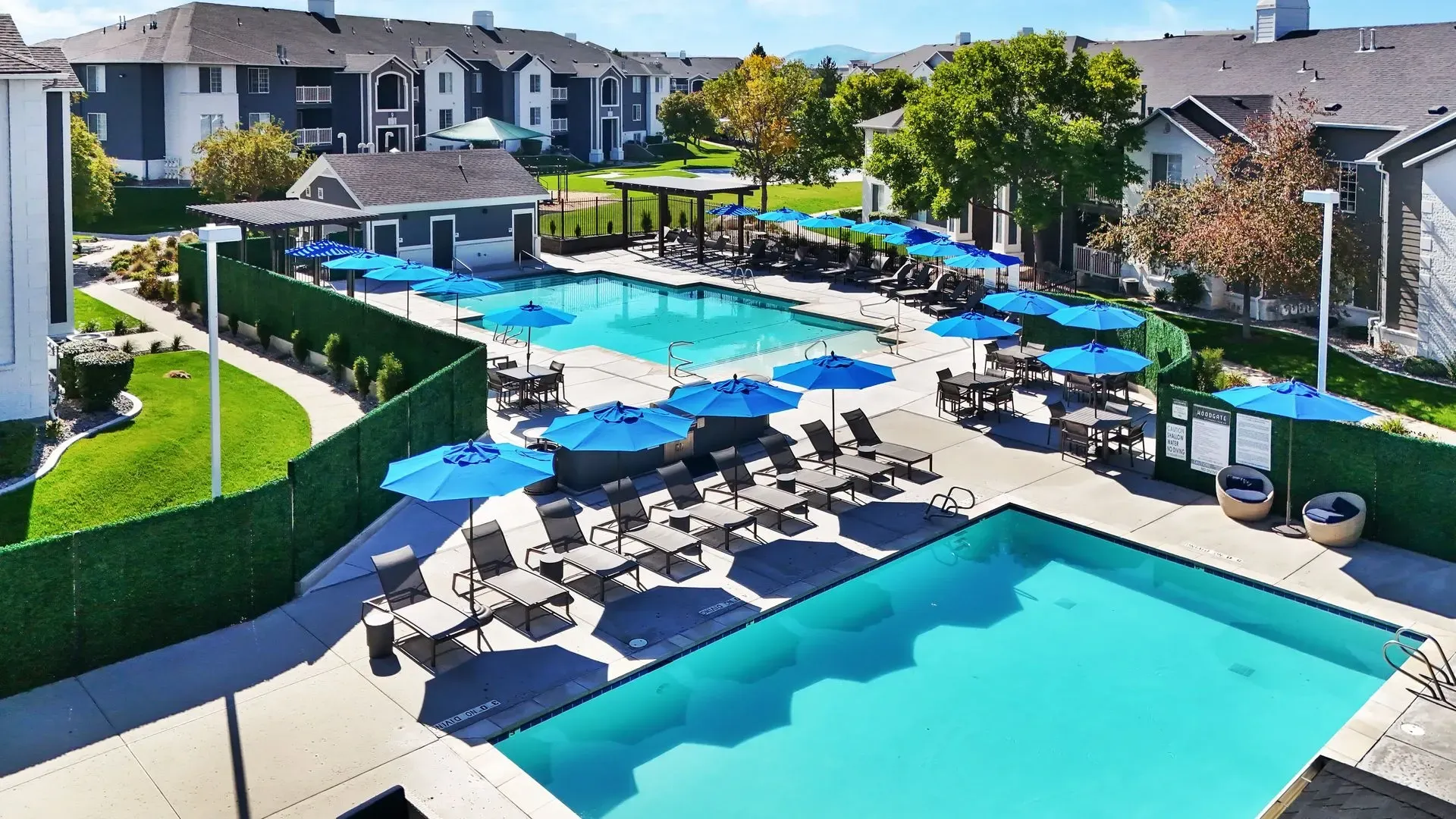 Luxury apartment complex with a large outdoor swimming pool, lounge chairs, umbrellas, and seating areas.