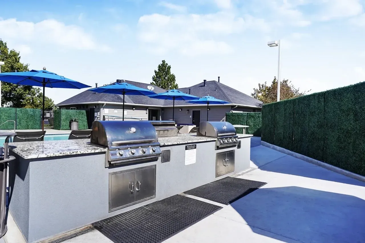 Outdoor kitchen with built-in grills and blue umbrellas next to a swimming pool.
