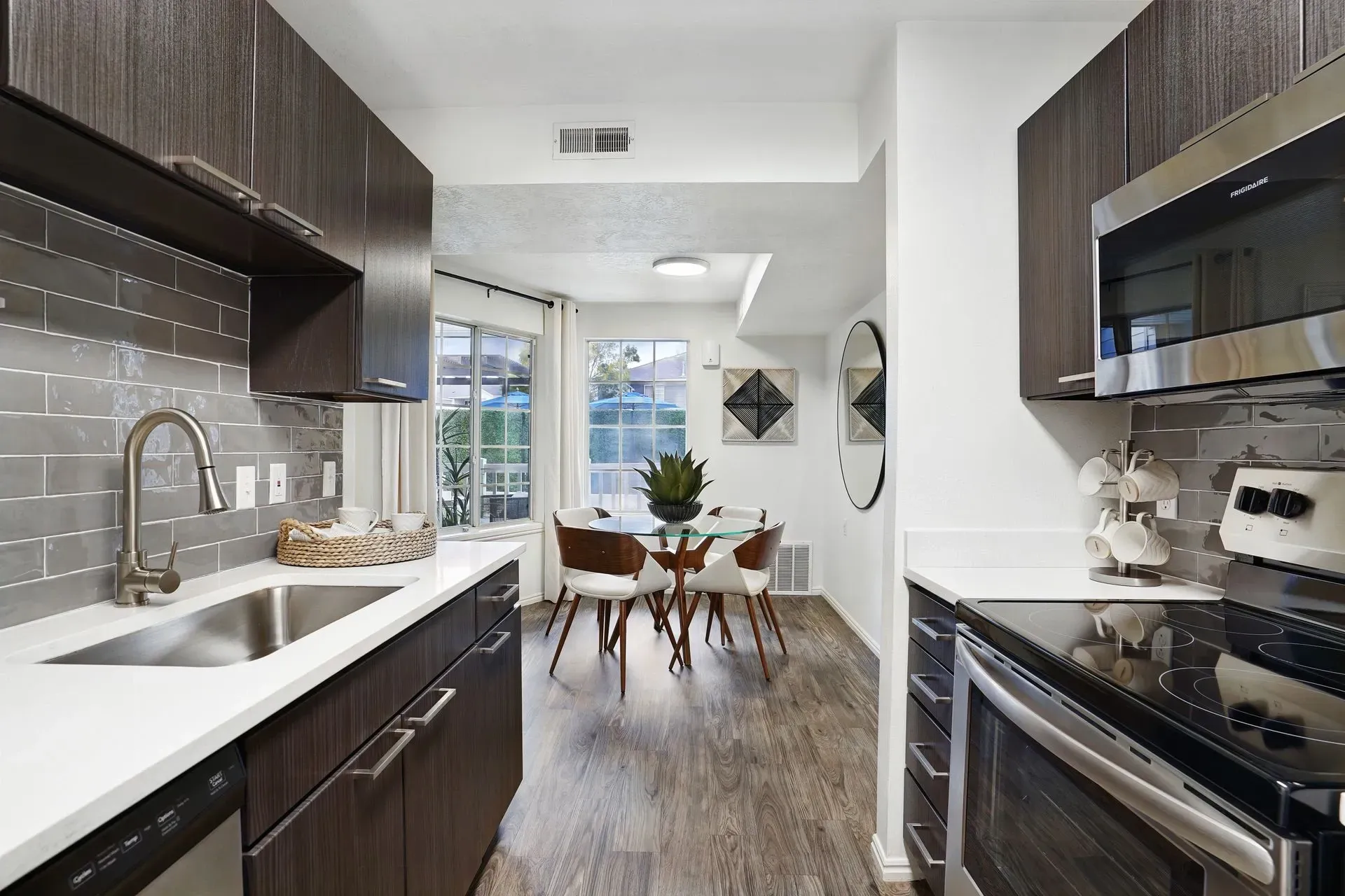 Modern kitchen and dining area with dark wood cabinets, stainless steel appliances, and a glass-top dining table.