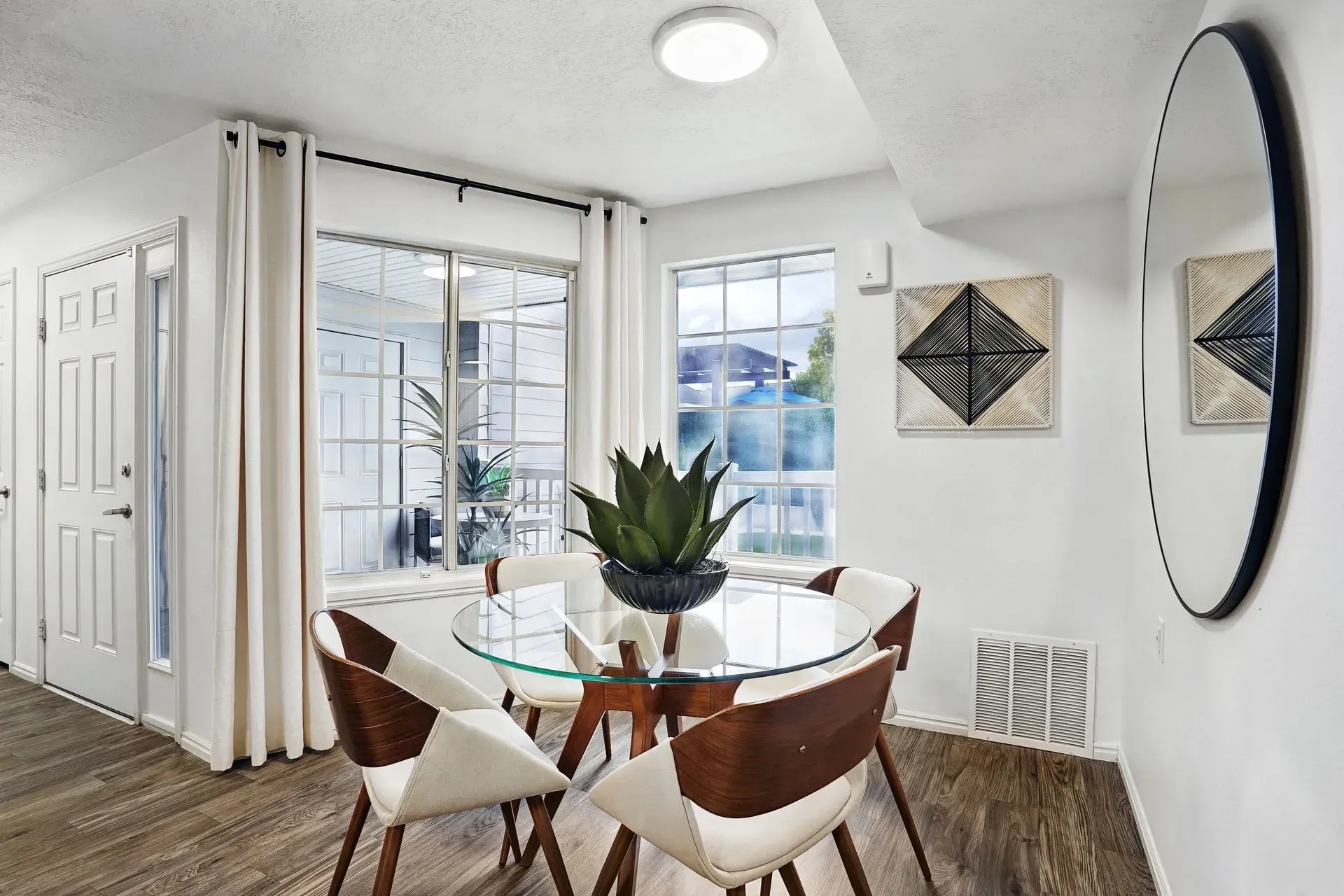 Dining area with a glass table and four chairs, next to a large window.