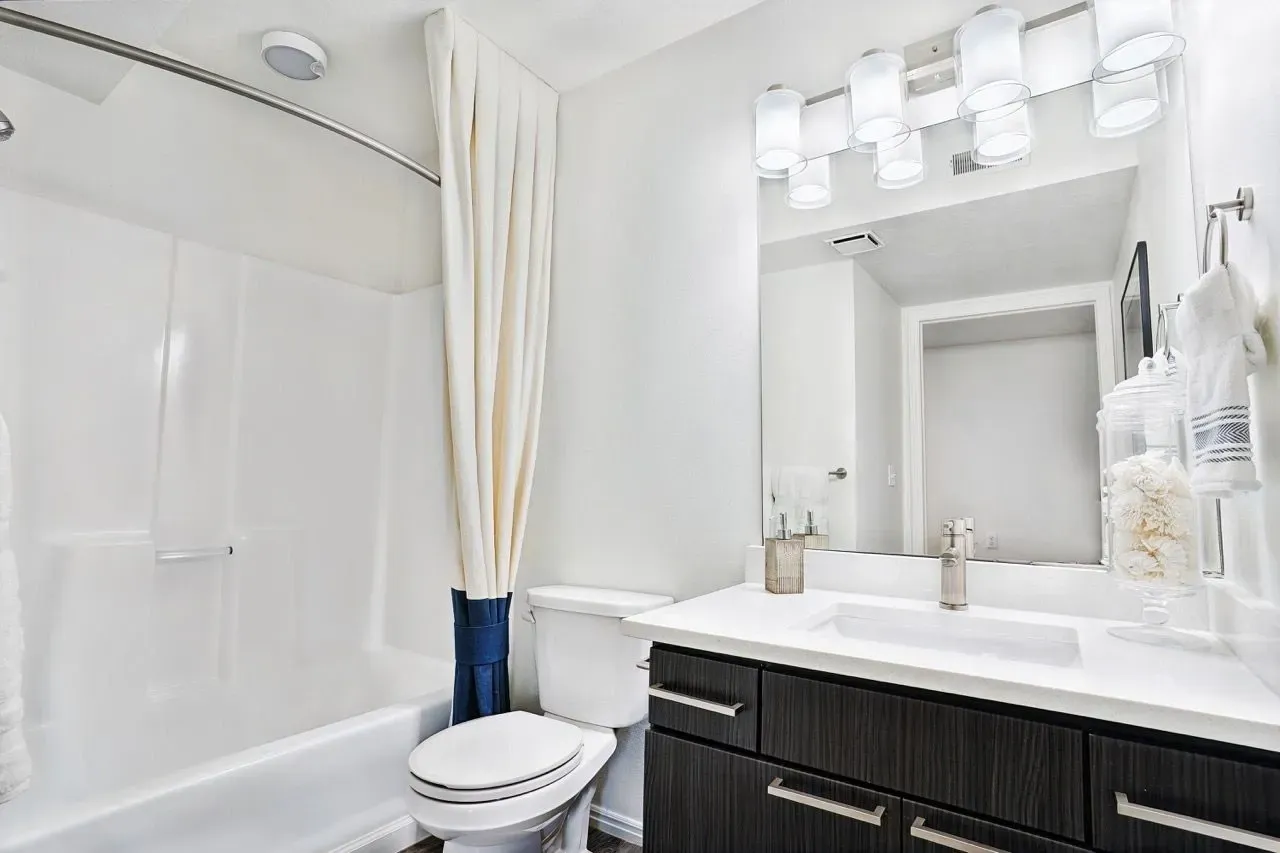 Modern bathroom with a white bathtub, toilet, and vanity with a sleek sink and ample counter space.
