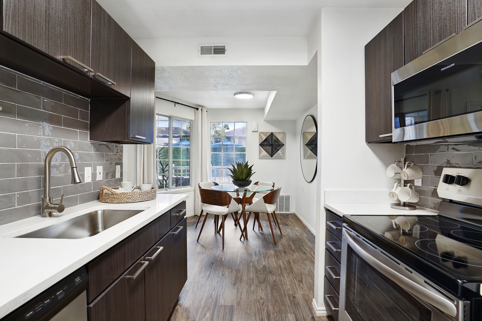 Modern apartment kitchen with dark wood cabinets, stainless steel appliances, and a glass dining table at Woodgate.