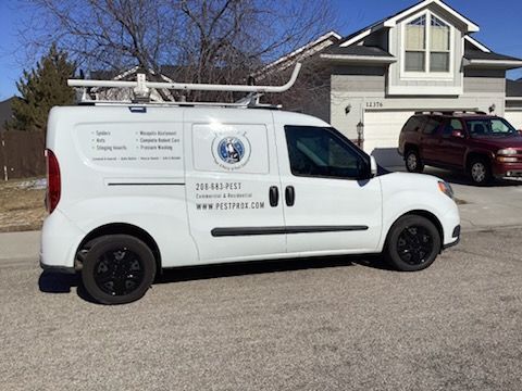 A white service van with business branding and a roof rack parked on a residential street next to a house.