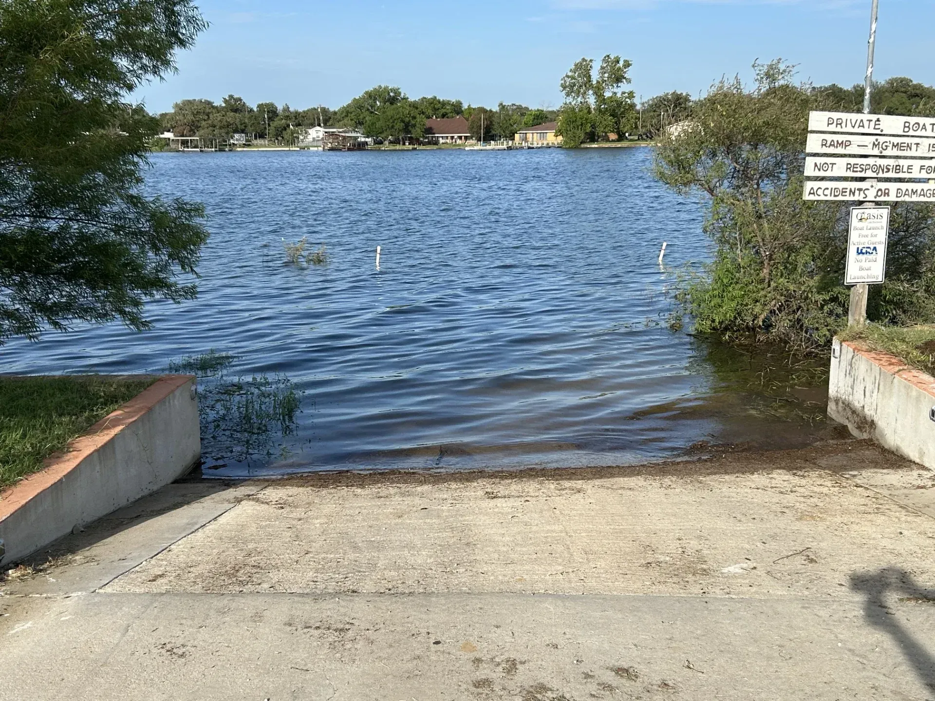 Boat ramp leading into calm blue lake with shore and signpost at right