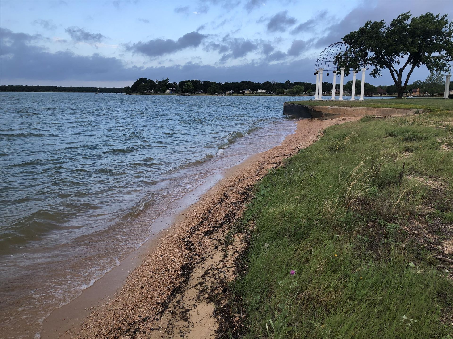 Rocky shoreline with waves, grassy bank, and white lampposts at dusk
