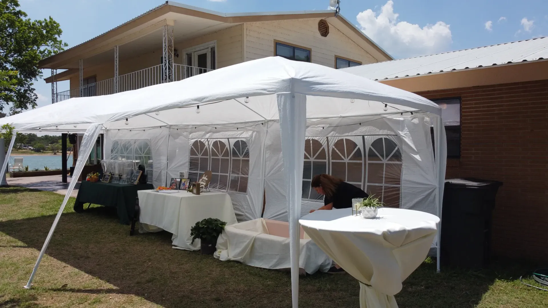White canopy tent set up outdoors beside a brick house, with tables and white tablecloths inside.