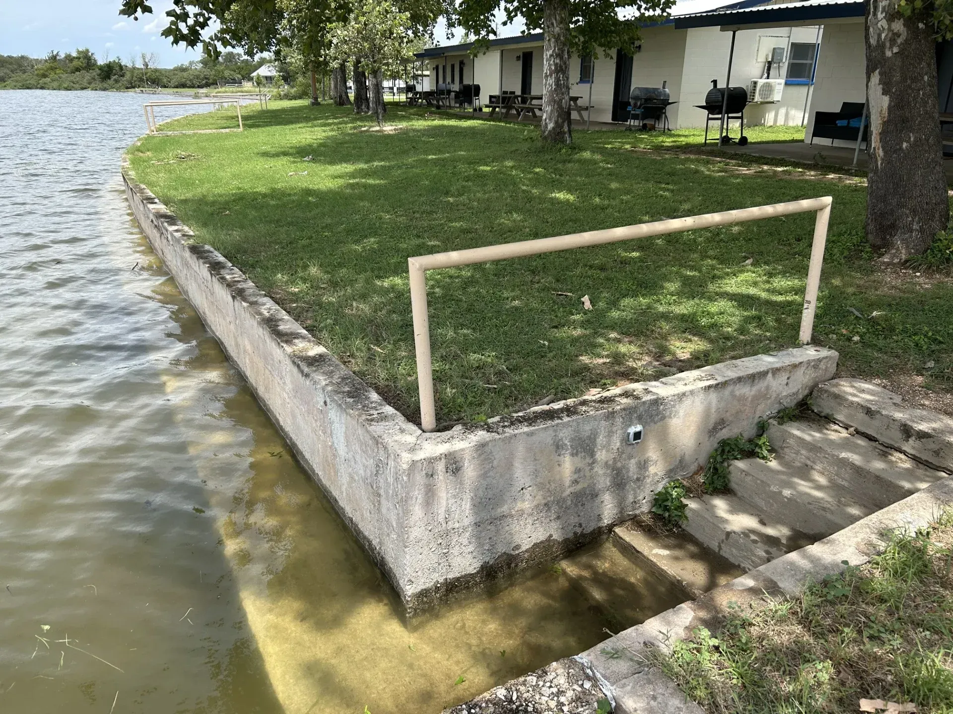 Concrete lakeside corner with grass, railing, and steps beside a building