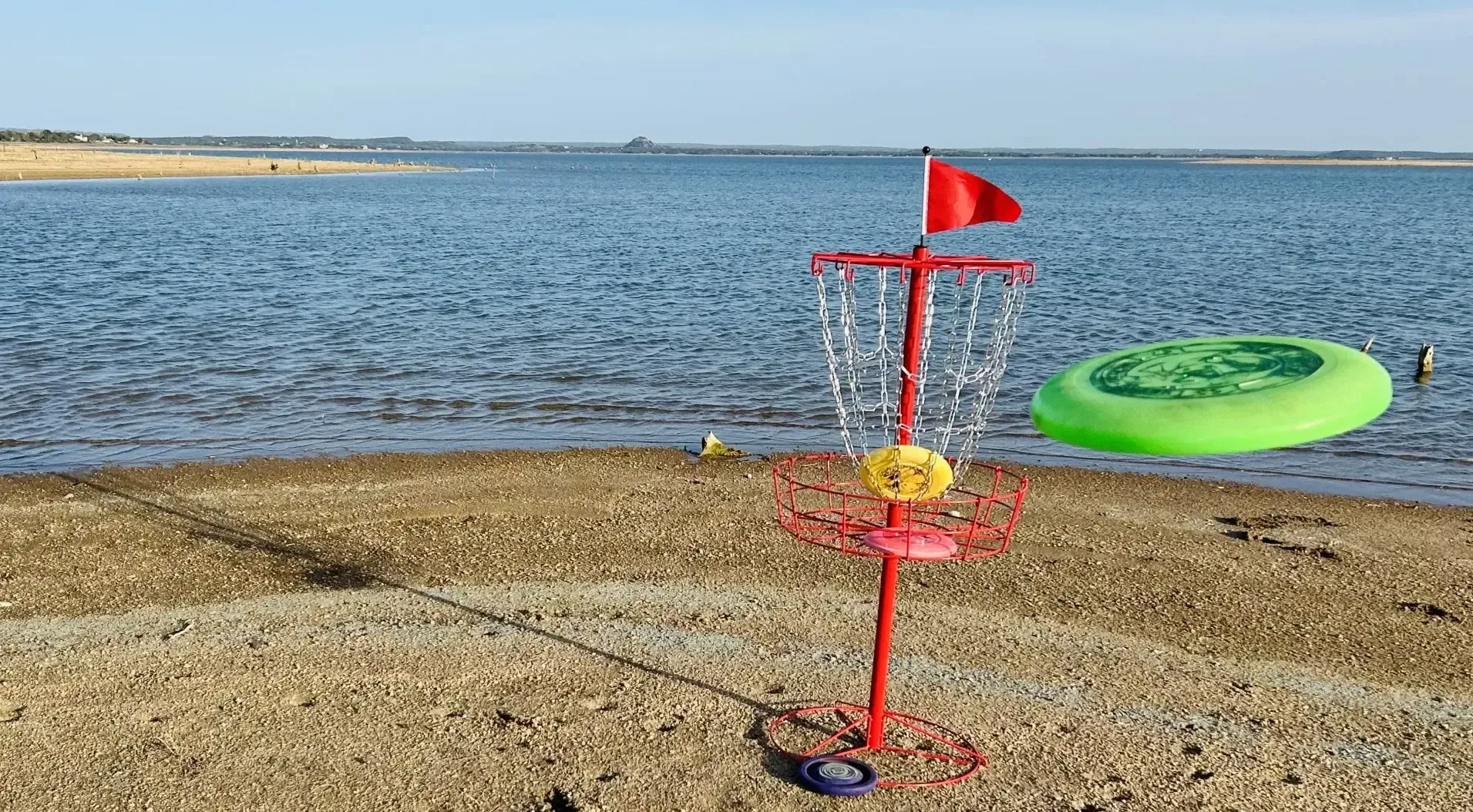 Beach toy and green inflatable ring on sandy shore beside calm blue water under a clear sky