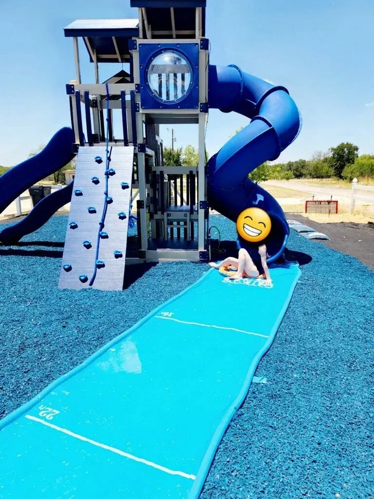 Child climbing at a blue playground with slides and a climbing wall under a clear sky