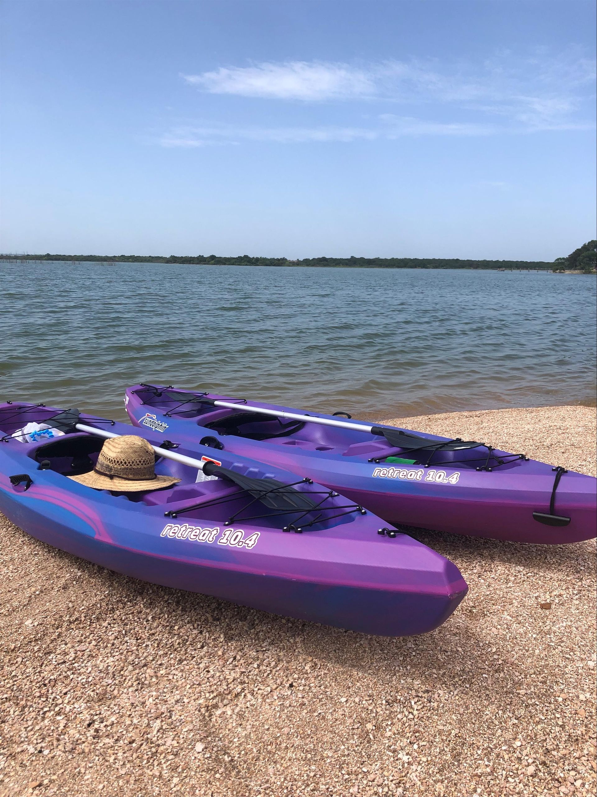 Two purple kayaks on a pebbled beach beside calm water under a clear blue sky
