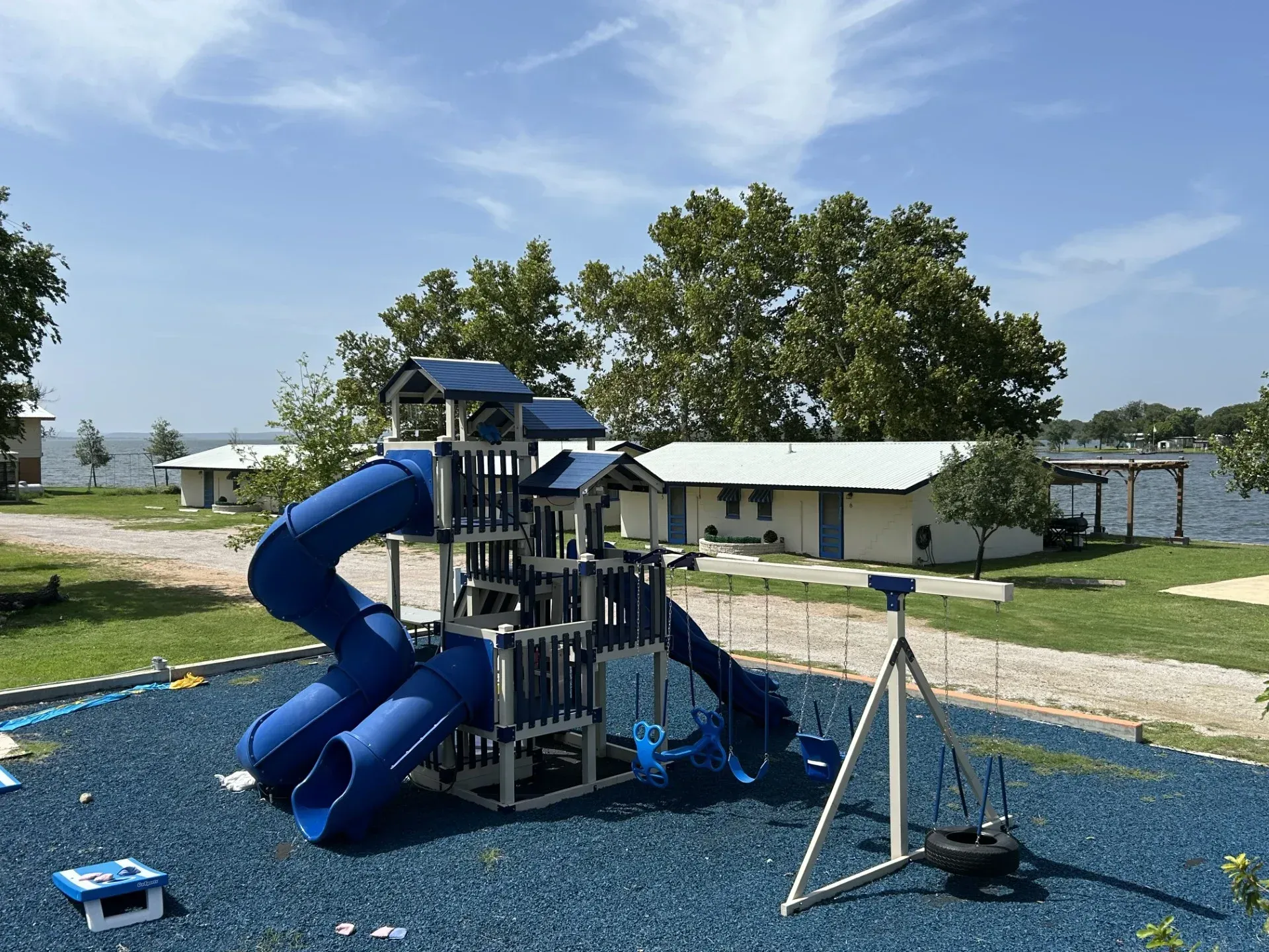 Blue playground slide and climbing structure on a rubber play surface beside a building and trees