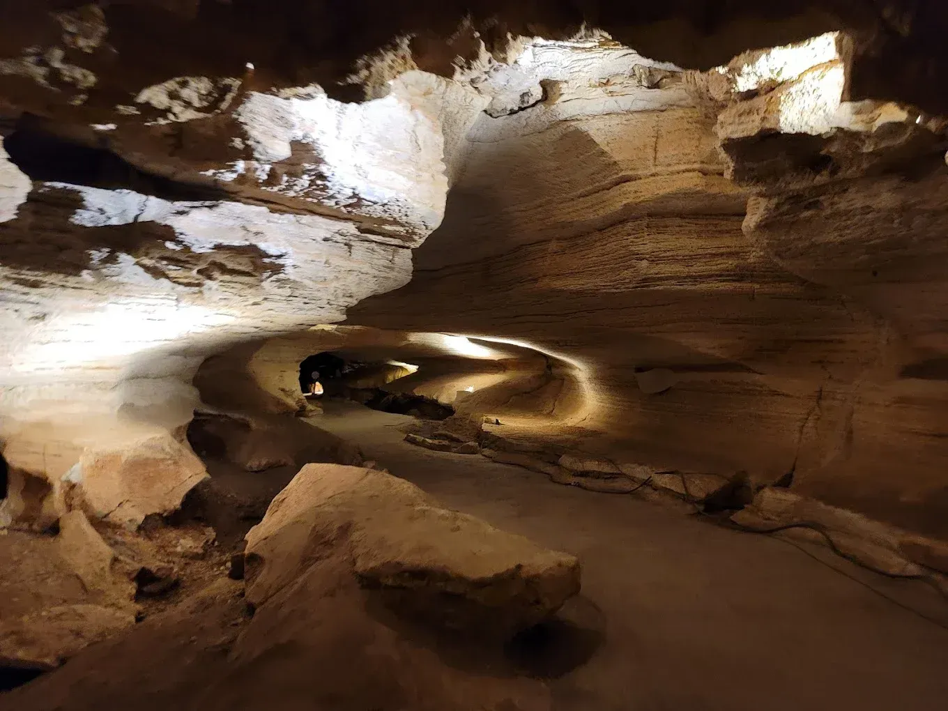 Dimly lit cave tunnel with layered rock walls and a sandy floor
