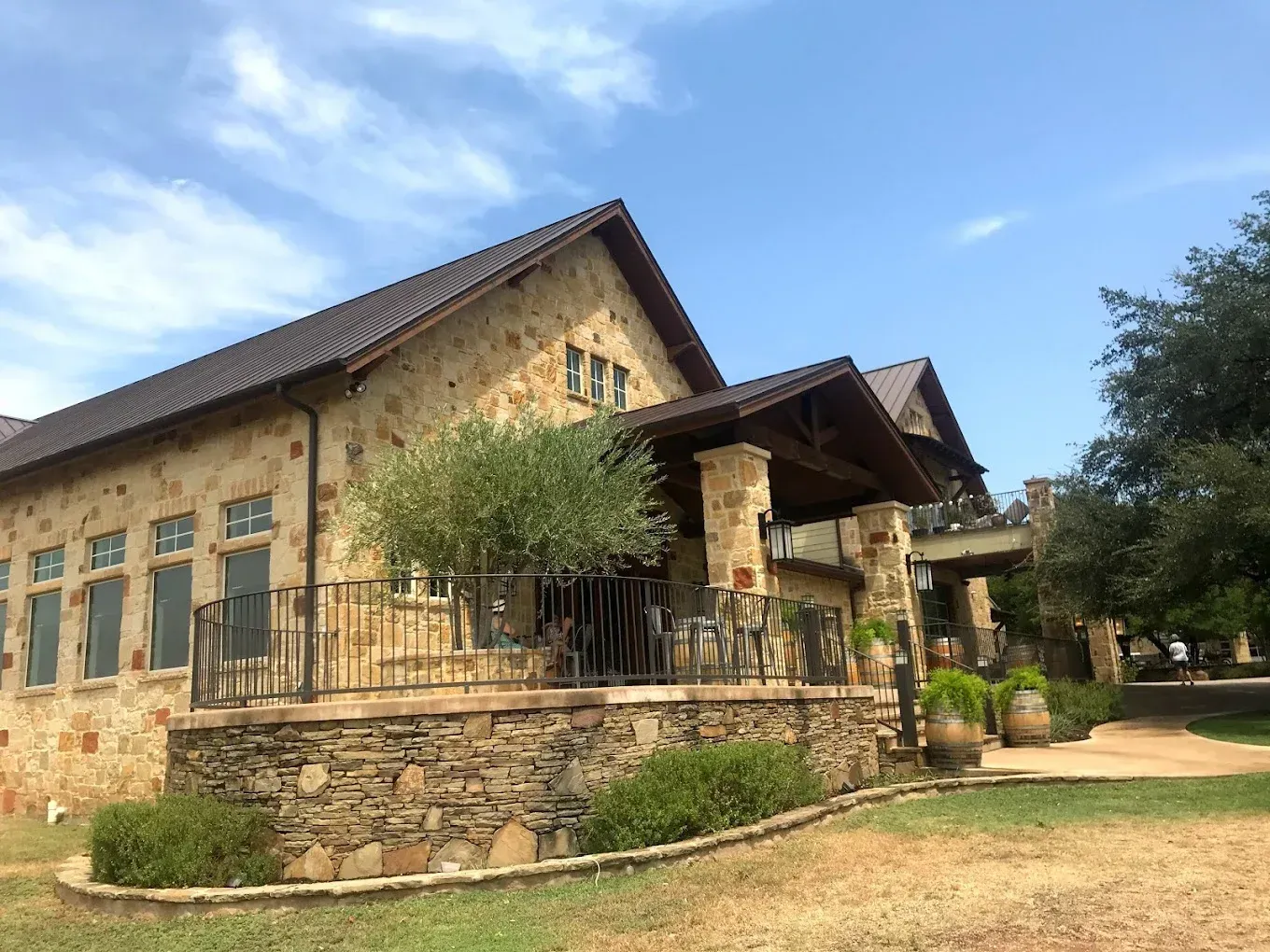Stone lodge with porch and green shutters under a blue sky, beside a dirt path and trees
