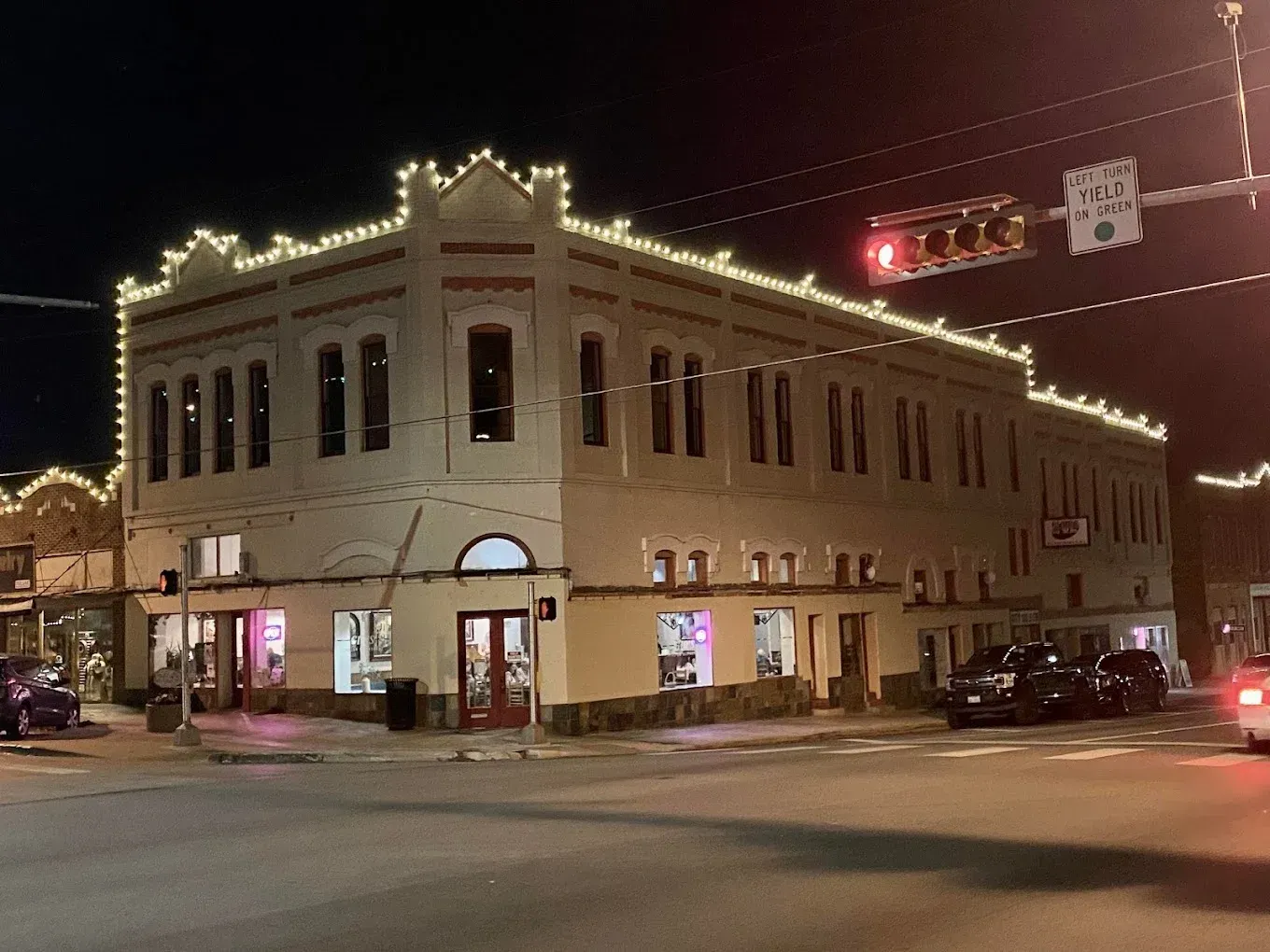 Historic corner building at night, outlined in white lights, with lit storefronts and street traffic.