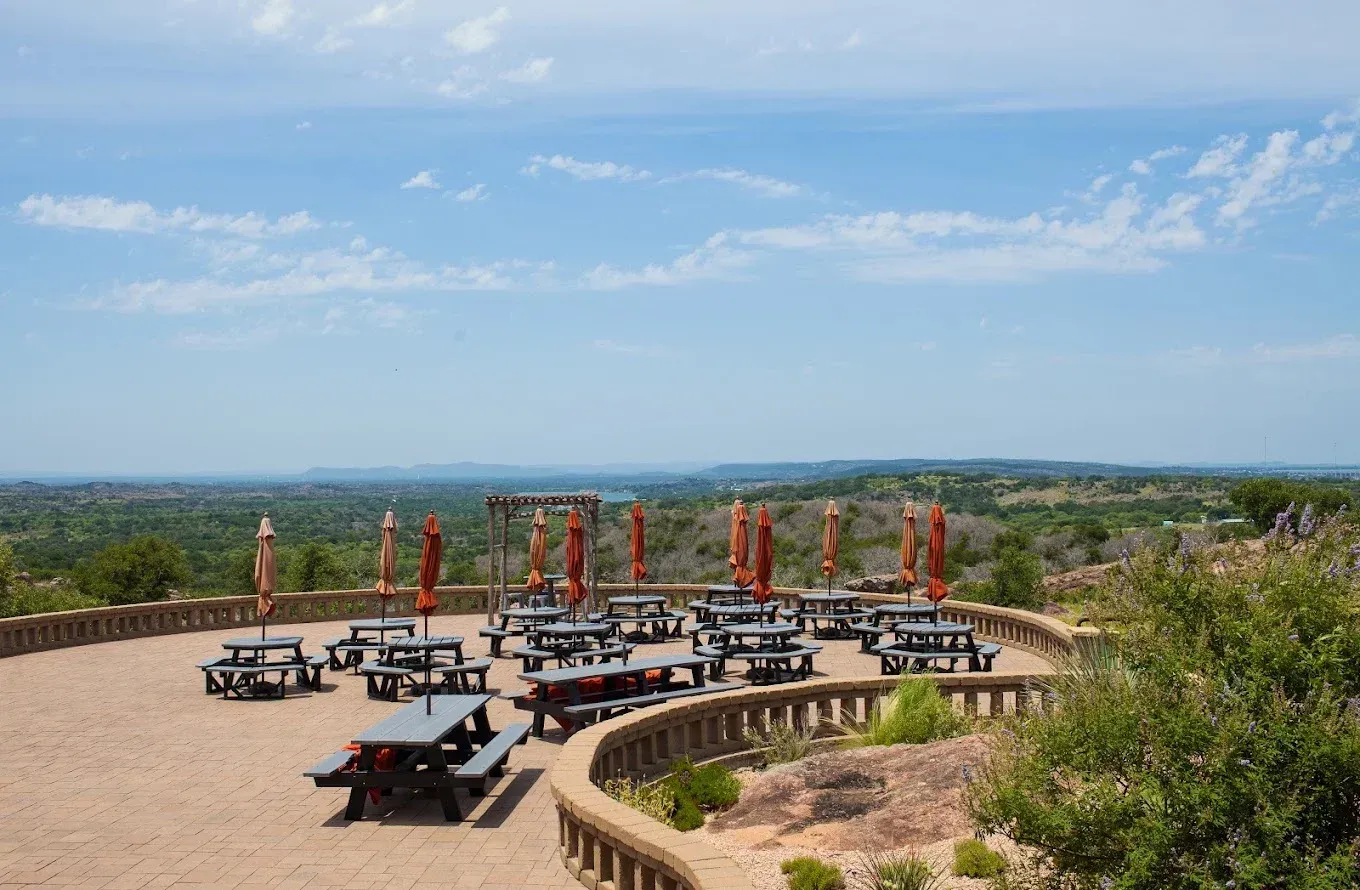Outdoor patio with picnic tables and orange umbrellas overlooking a wide scenic landscape