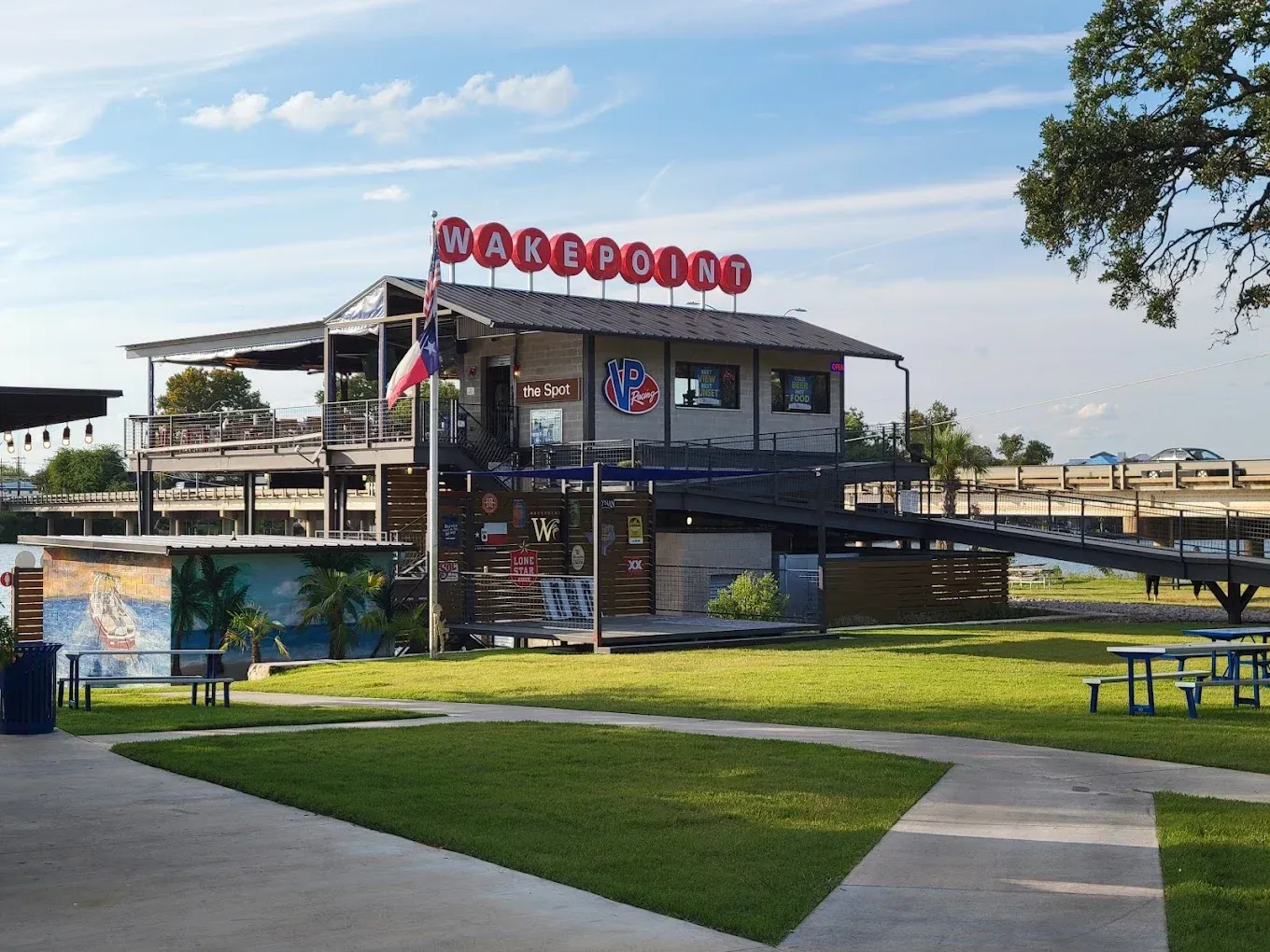 Modern floating restaurant with red sign, on calm water beside a grassy park and walkway