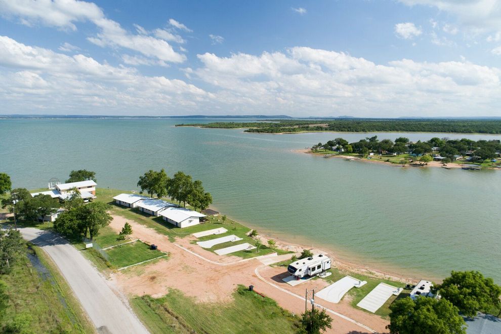 Aerial view of a lakeside campsite with white tents, trees, and calm water under a cloudy sky