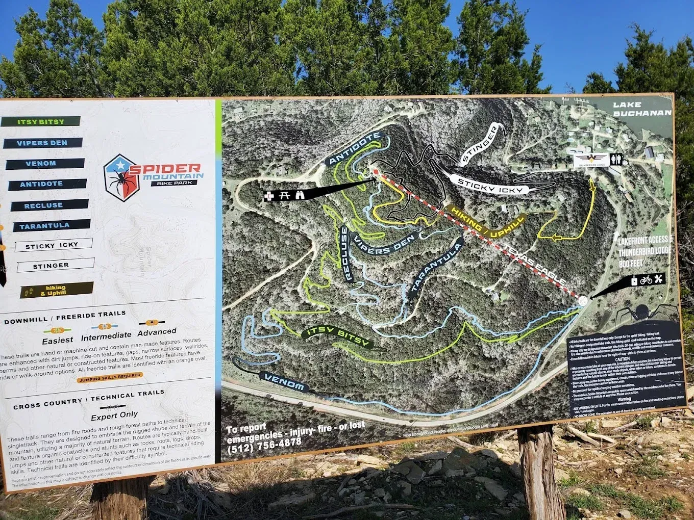Trail map signboard with route lines and trail information posted outdoors among trees