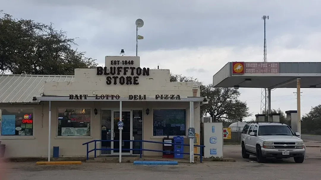 Blue Dot Donuts storefront with drive-thru, blue benches, and a white pickup at the pump nearby