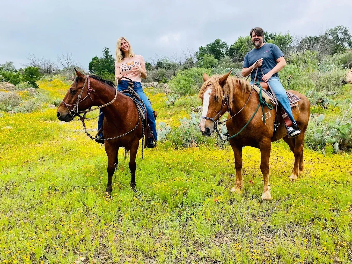 Two people riding horses in a green field with yellow wildflowers