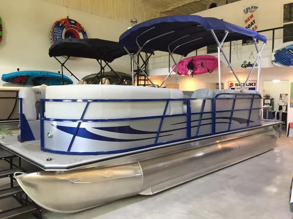 Pontoon boat with blue trim and black canopy displayed indoors in a showroom