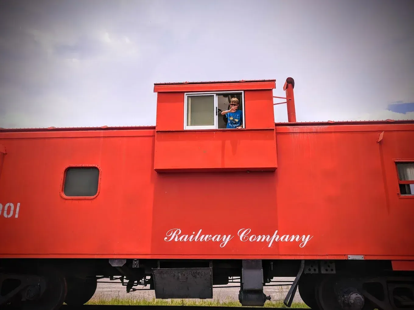 Red railway caboose with a person in the window under a cloudy sky