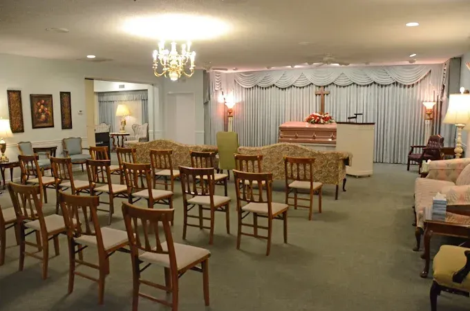 Funeral home chapel with rows of chairs facing a casket and podium on a stage, soft lighting.