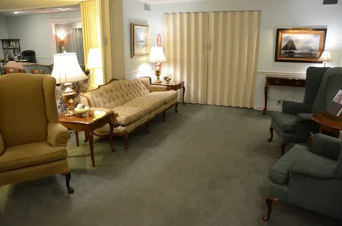 Funeral home waiting area, with a sofa, chairs, tables, lamps, and artwork.