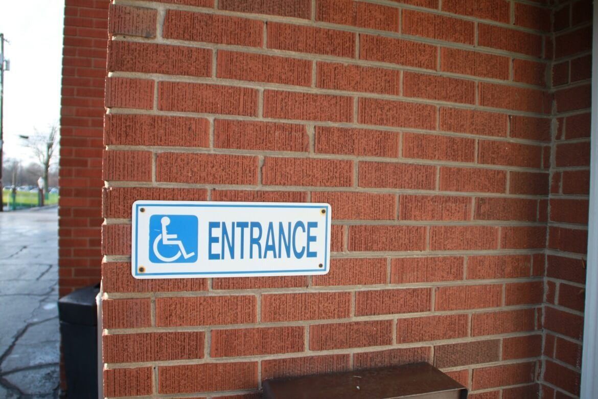 Blue and white handicap accessible entrance sign on a brick wall.