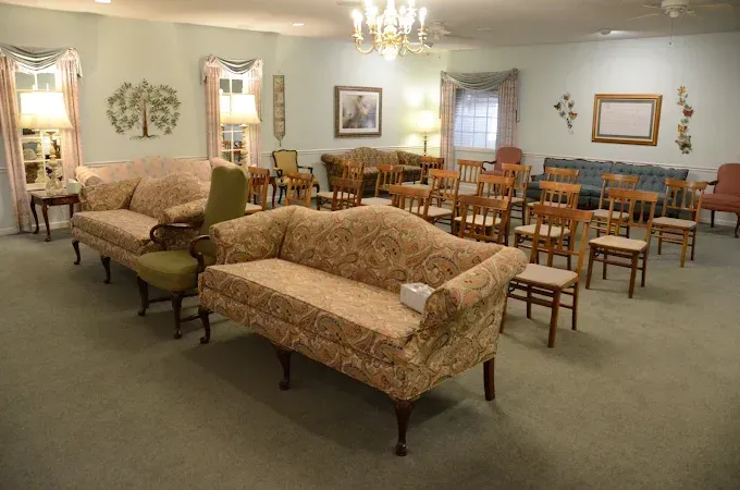 A room in a funeral home with seating, including couches and chairs, light colors, and soft lighting.