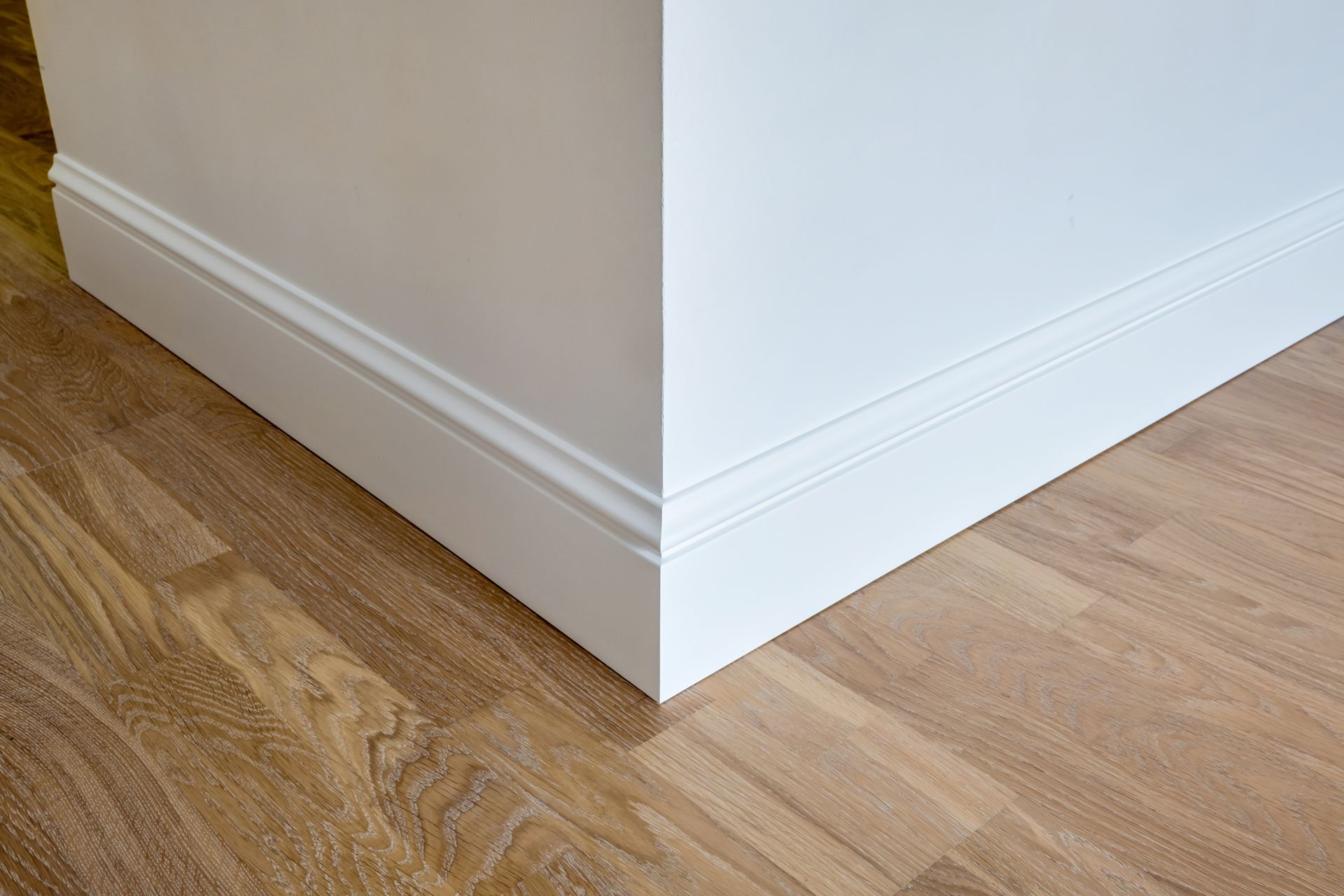 A close up of a white skirting board on a wooden floor.