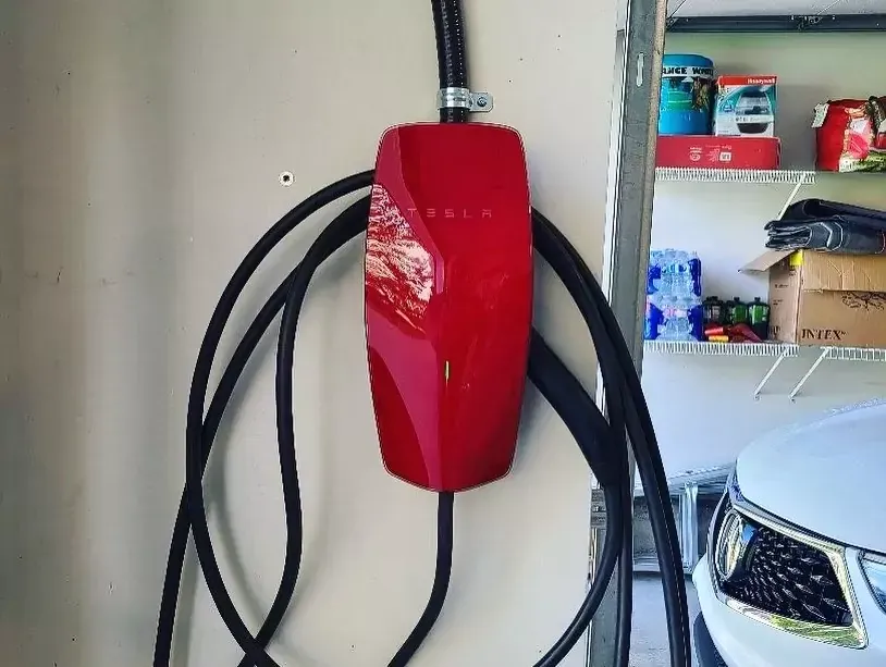 Red Tesla wall charger mounted on a wall with black cable. Garage setting.