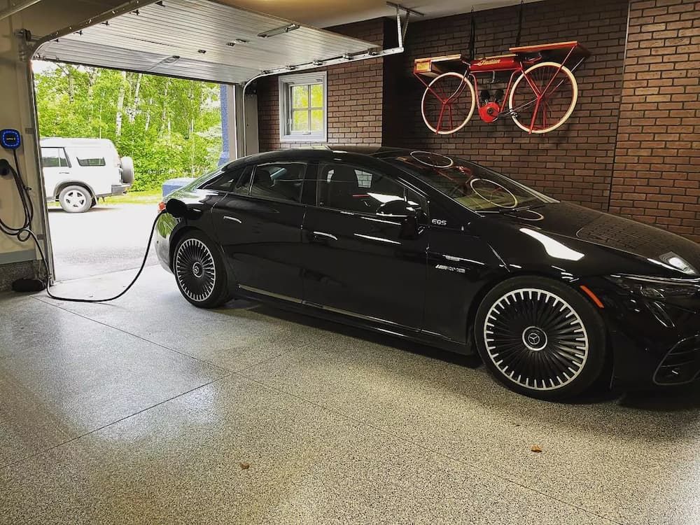 Black Mercedes-Benz EV charging in a garage with a decorative bicycle sign and an open door.
