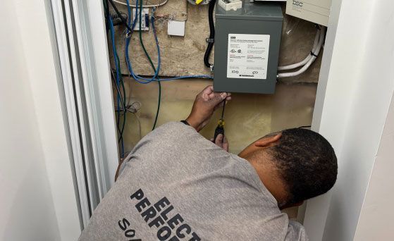 Person working on electrical panel in a recessed wall. Wires and equipment visible.