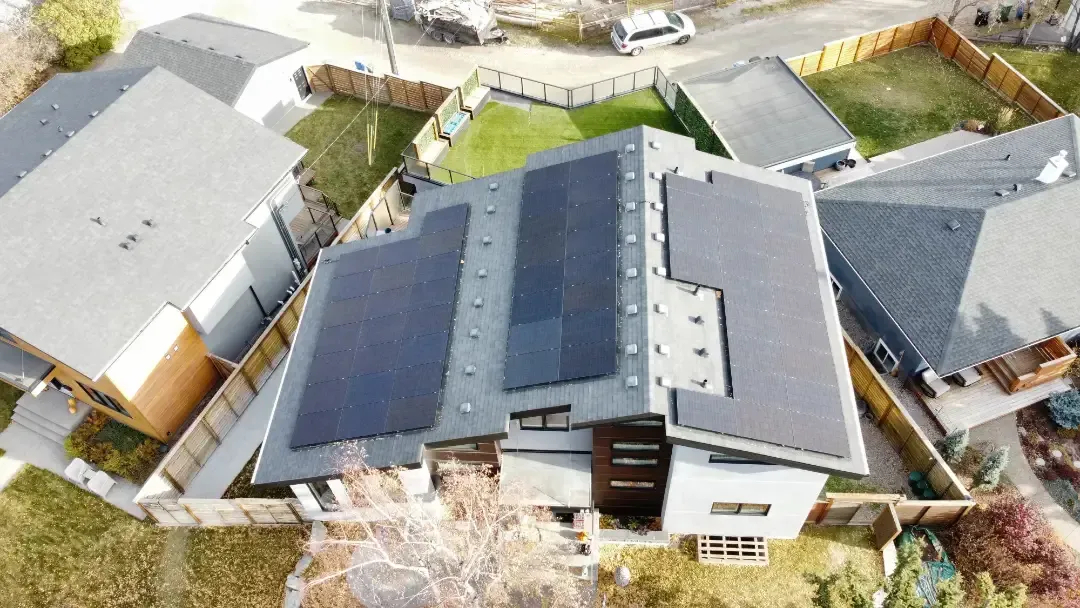 Aerial view of a house with solar panels on the roof surrounded by other houses and a lawn.
