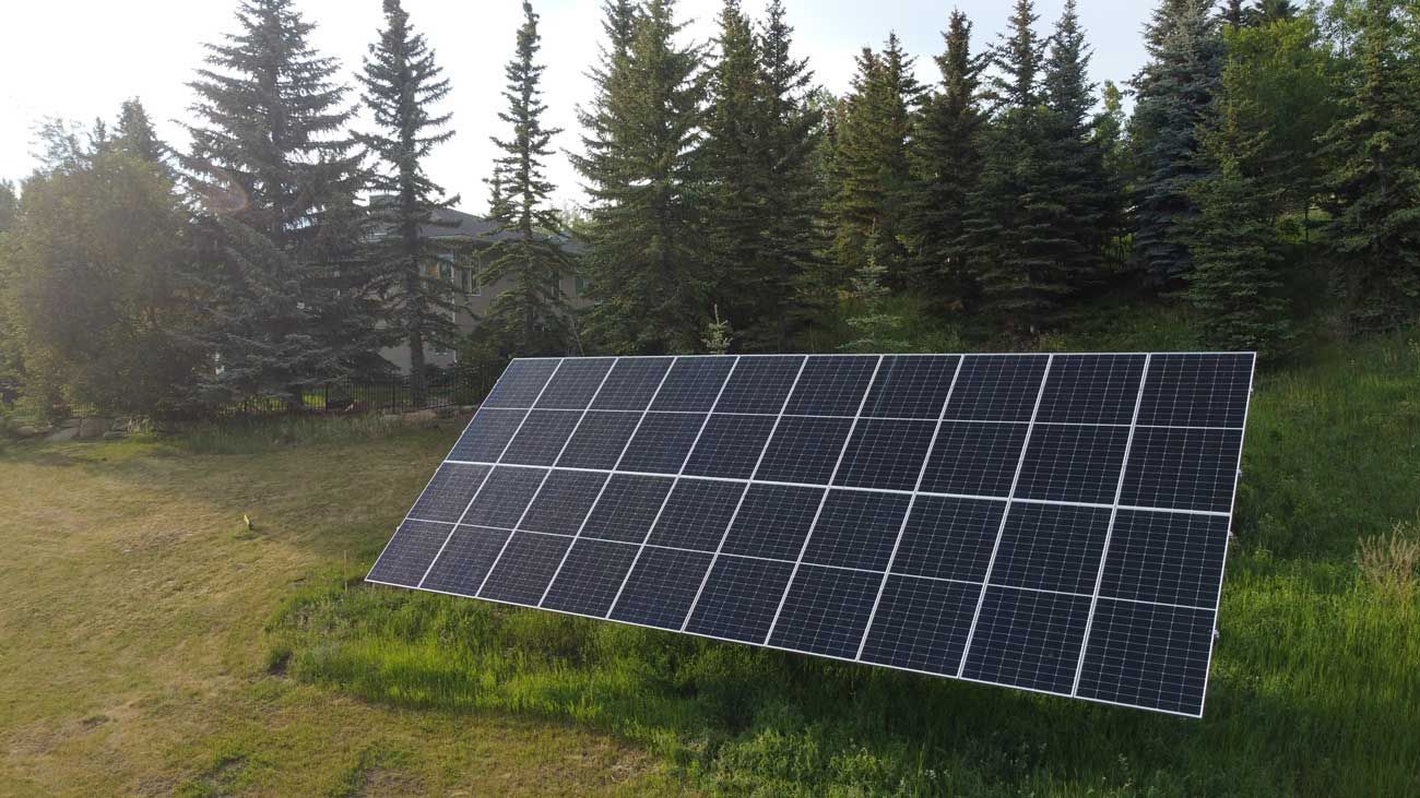 Solar panel array angled towards the sky, set in a grassy yard with trees in the background.