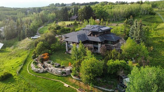 House with stone exterior and black roof, nestled among trees on a hillside.